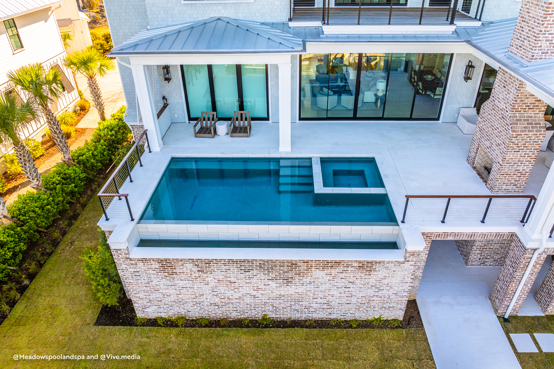 Elevated pool terrace connected to indoor spaces through large sliding glass doors in a modern coastal home.