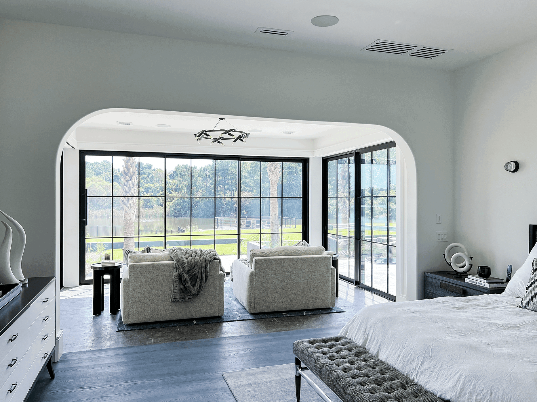 Bedroom seating area with expansive black-framed sliding glass doors opening to serene outdoor views.